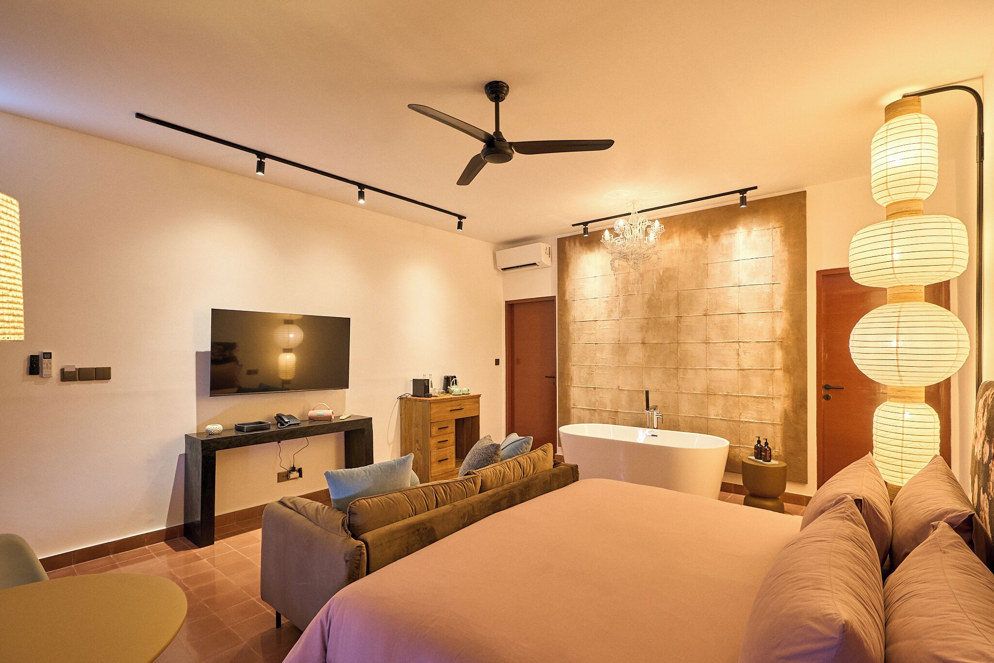 A modern bedroom with a large bed, a flat-screen TV, a desk, a sofa, a bathtub, and a ceiling fan.