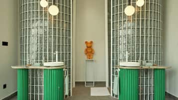 A bathroom with two mirrored glass partitions, green cylindrical stools, a central bear sculpture, and round pendant lights.
