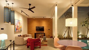 A modern living room with a sofa, red chairs, a glass table, and a ceiling fan. - HOTEL EDEN UBUD (Ubud)
