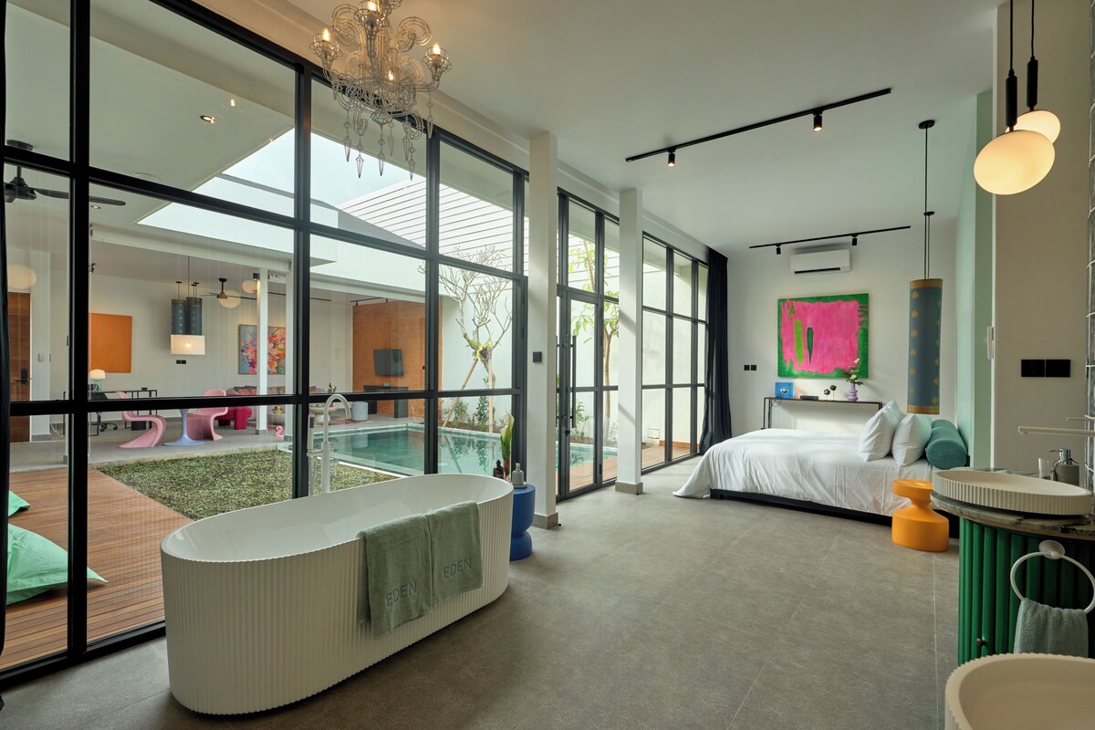 A modern bedroom with a large window, a bathtub, a bed, and a bathroom with a sink and mirror.