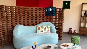 A modern living room with a blue sofa, round coffee tables, and a wooden wall. - HOTEL EDEN UBUD (Ubud)