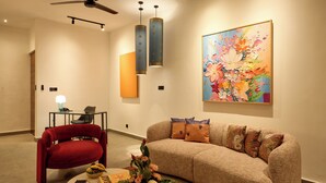 A modern living room with a red chair, a beige sofa, a painting, and pendant lights. - HOTEL EDEN UBUD (Ubud)