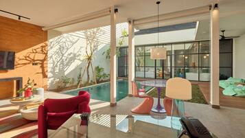 Una sala de estar moderna con una mesa de vidrio, un sofá rojo y vistas a la piscina.