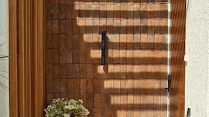 A narrow outdoor corridor with a wooden slatted ceiling, a brick wall, and a potted plant. - HOTEL EDEN UBUD (Ubud)