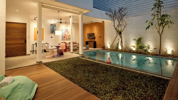 A modern outdoor pool area with a wooden deck, a seating area with a sofa and chairs, and a TV mounted on the wall. - HOTEL EDEN UBUD (Ubud)