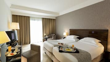 A hotel room with a large bed, a desk with a computer, a chair, and a tray with breakfast items.