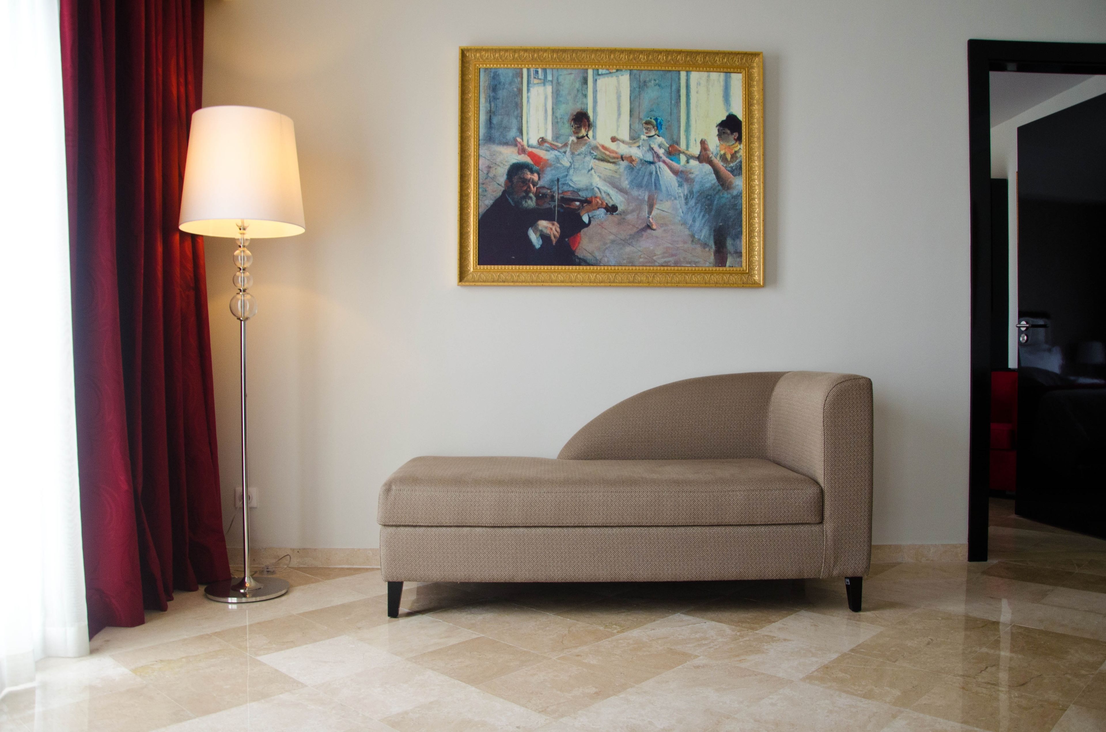 Een kamer met een beige bank, een staande vloerlamp en een schilderij aan de muur.
