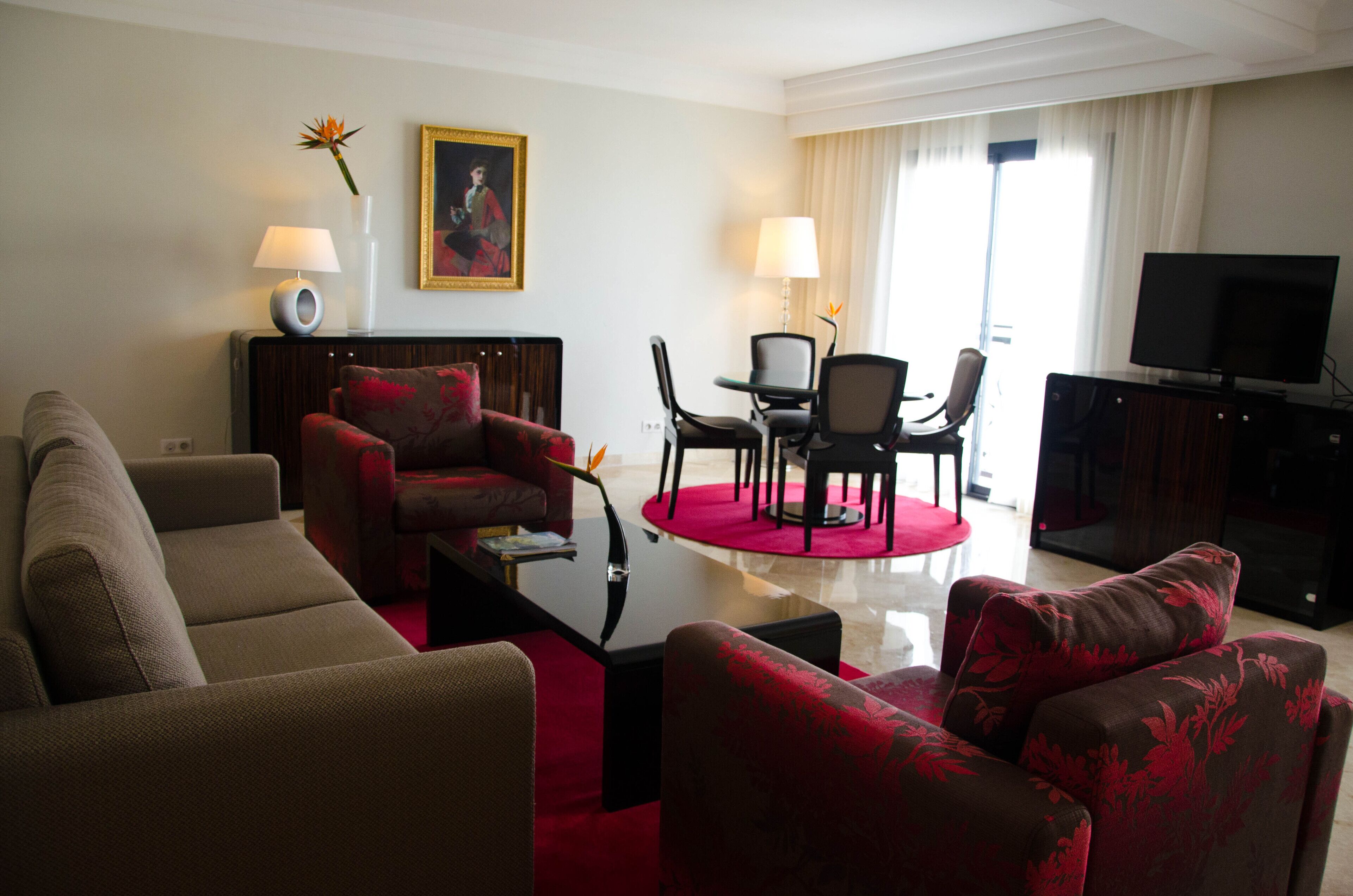 Une chambre d’hôtel dotée d’un espace salon comprenant un canapé, des fauteuils, une table basse et un téléviseur.