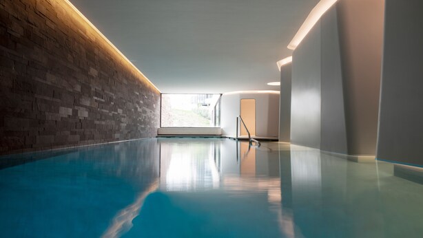 A modern indoor swimming pool with a brick wall and a glass door leading outside. - Hôtel Les Haras By Stay Collection (Strasbourg)