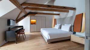 A modern bedroom with a large bed, a desk, and a chair. There is a door with a light in the background. - Hôtel Les Haras By Stay Collection (Strasbourg)