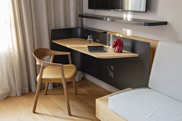 Un espacio habitable moderno con una silla de madera, una mesita, un objeto decorativo rojo y un sofá gris.