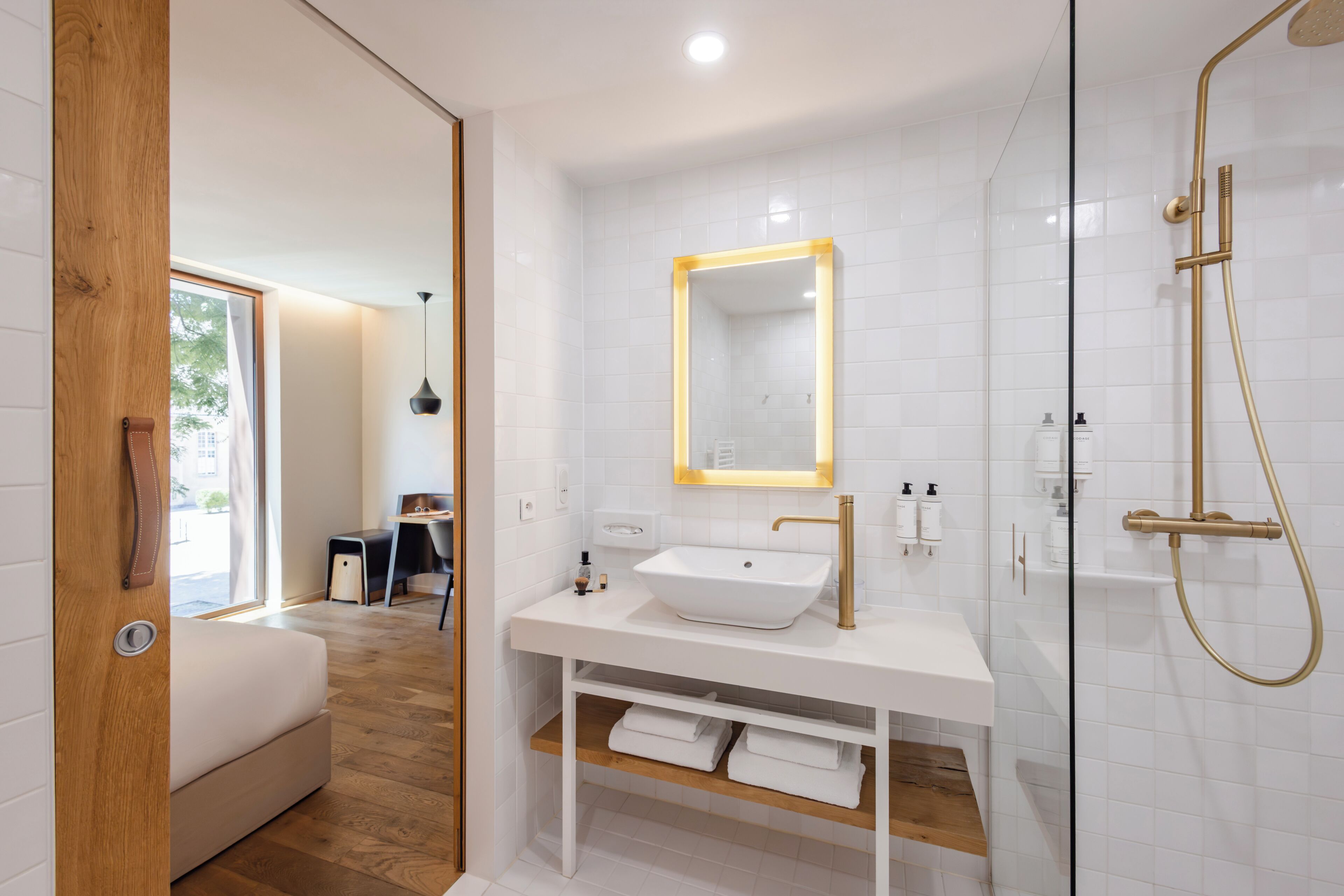 Un baño moderno con tocador blanco, un espejo grande y grifería de ducha dorada.