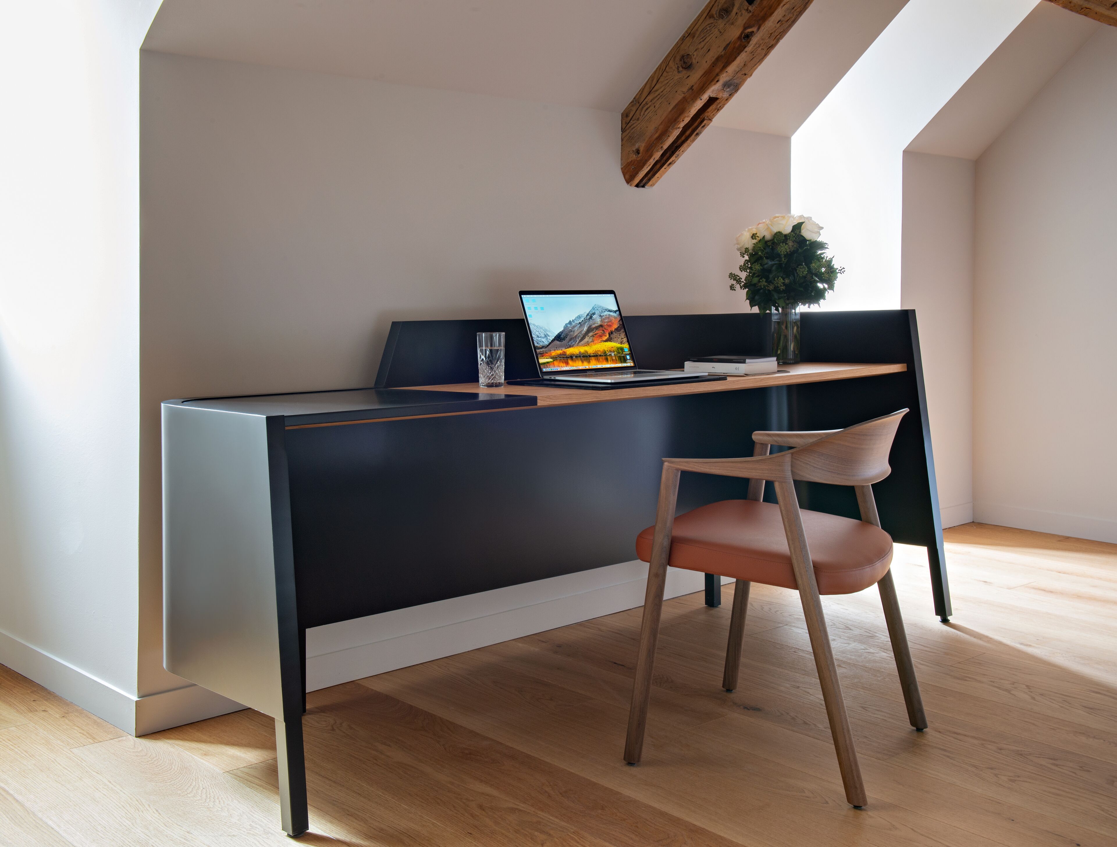 A modern office space with a desk, chair, laptop, and a vase with flowers.