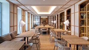 A modern interior with a central dining table, multiple seating arrangements, and a view of a kitchen area. - Hôtel Les Haras By Stay Collection (Strasbourg)
