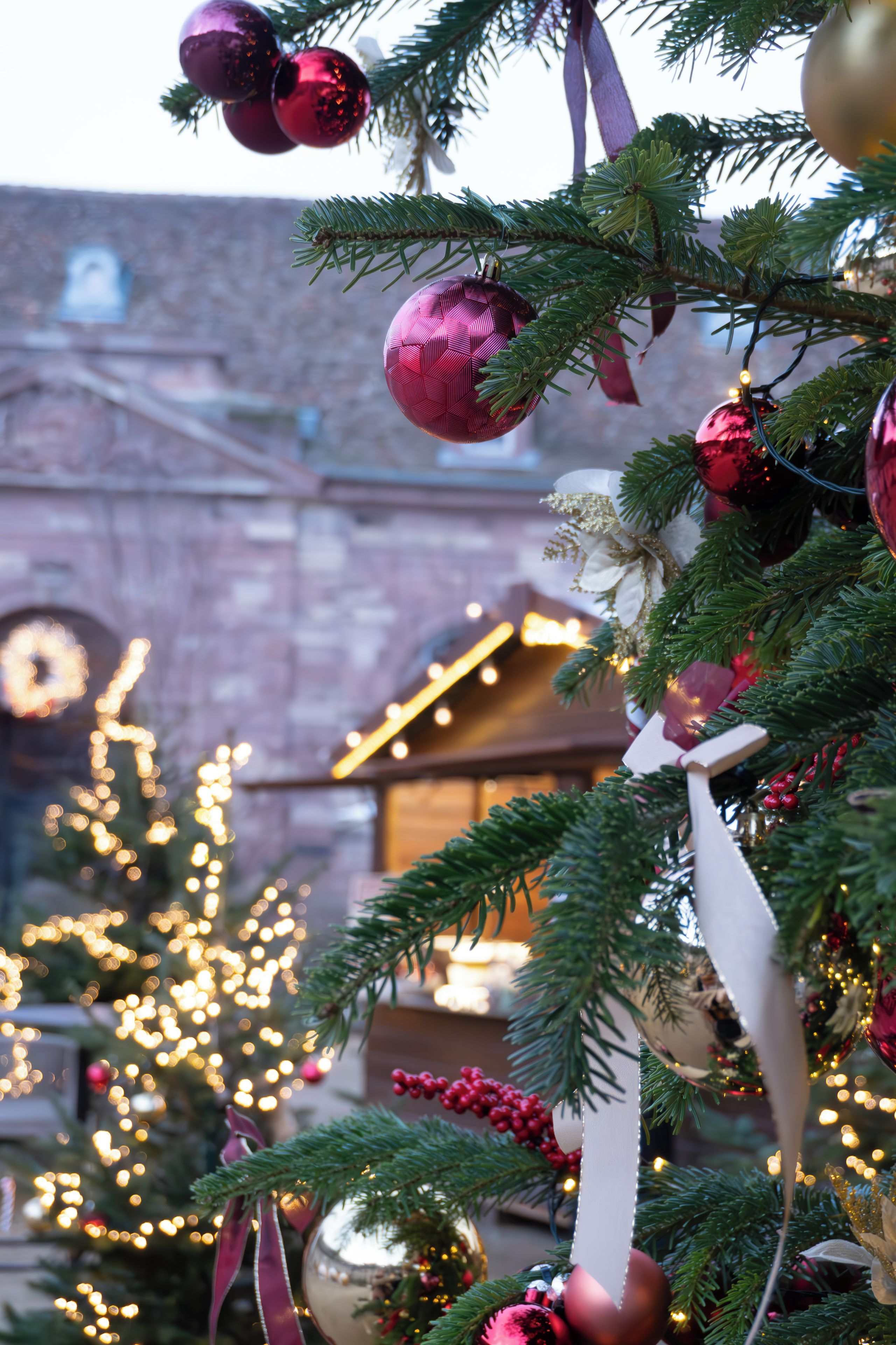 A Christmas tree with ornaments and lights, set against a building with a clock.