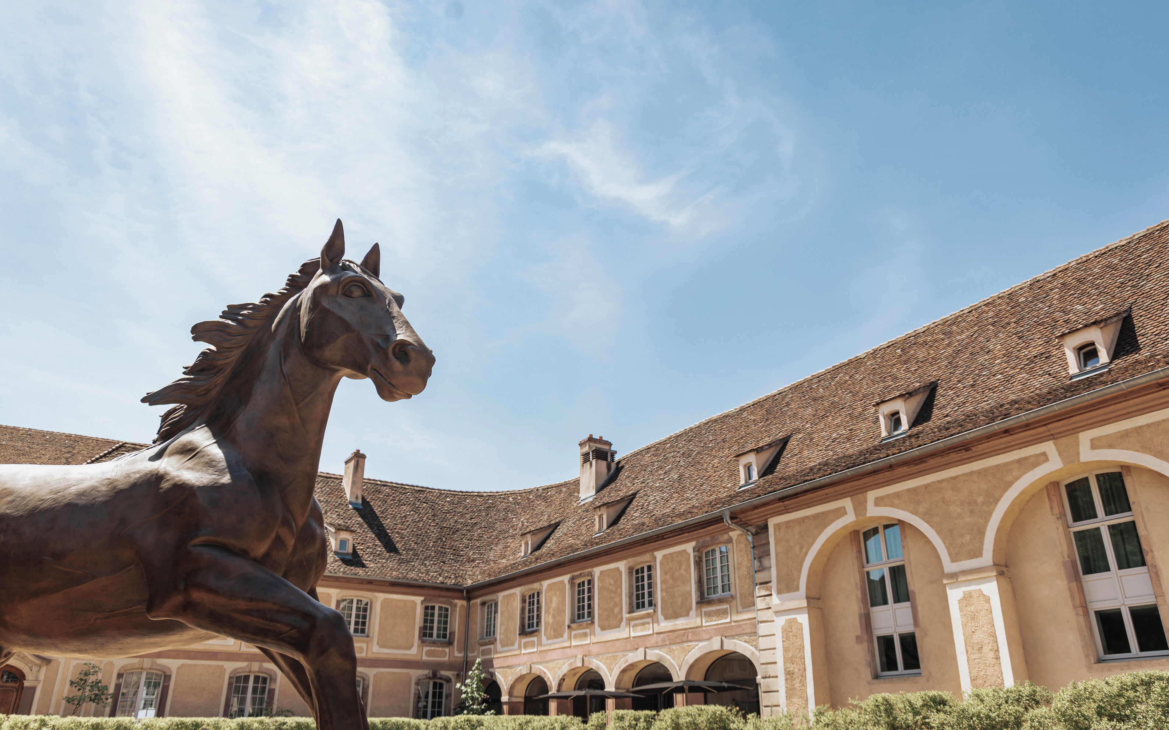 A courtyard with a bronze horse statue, a building with a tiled roof, and arched windows.