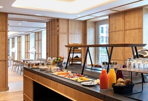 Montaje de desayuno tipo buffet con diversos alimentos, bebidas y disposición de mesas en un interior moderno.