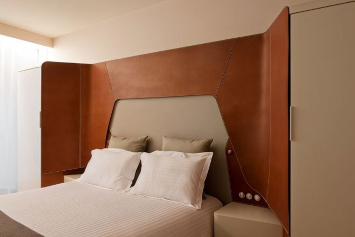 A modern hotel room with a large bed, two pillows, and a headboard with a unique design.