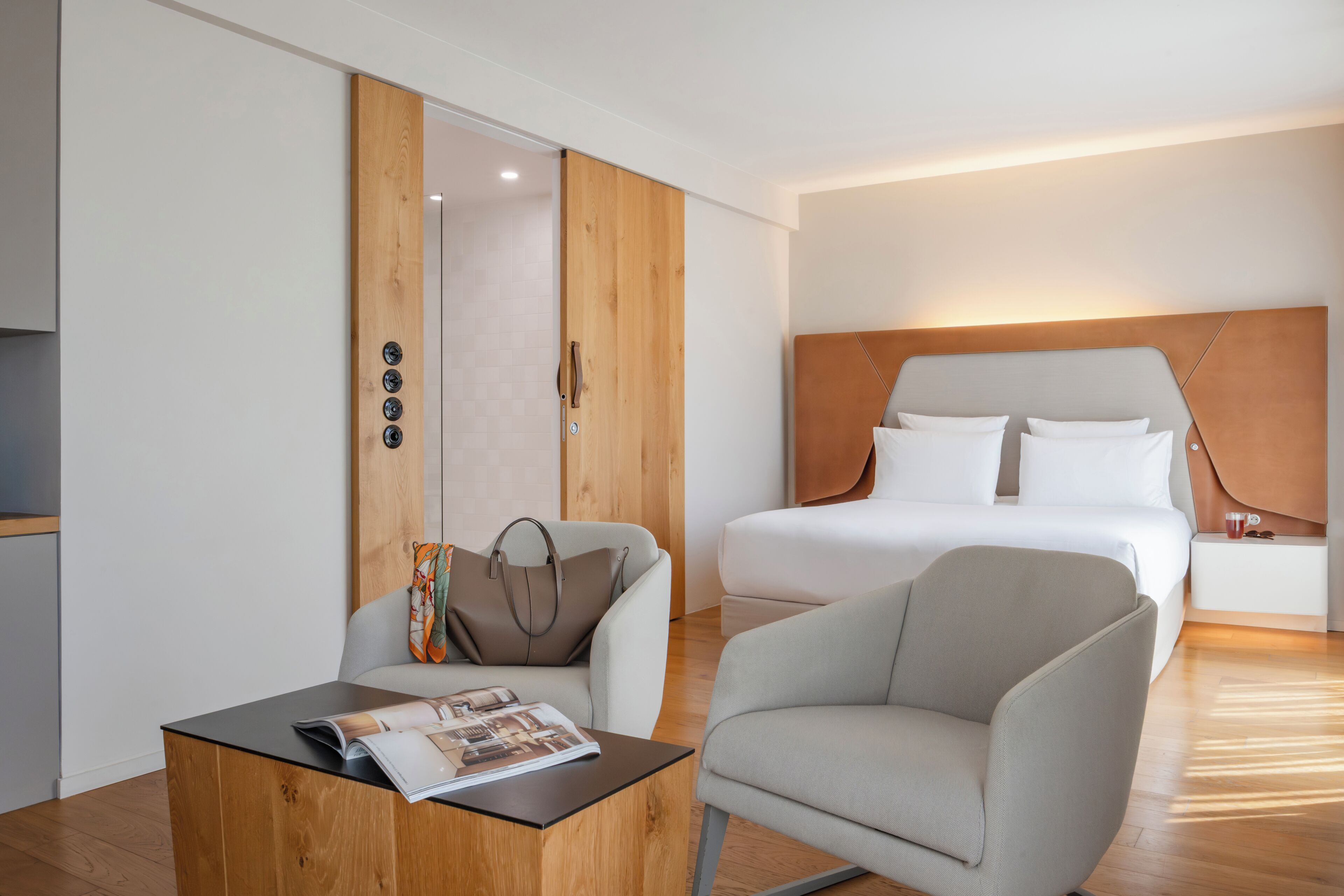 Una habitación de hotel moderna con una cama, zona de estar y un armario de madera.