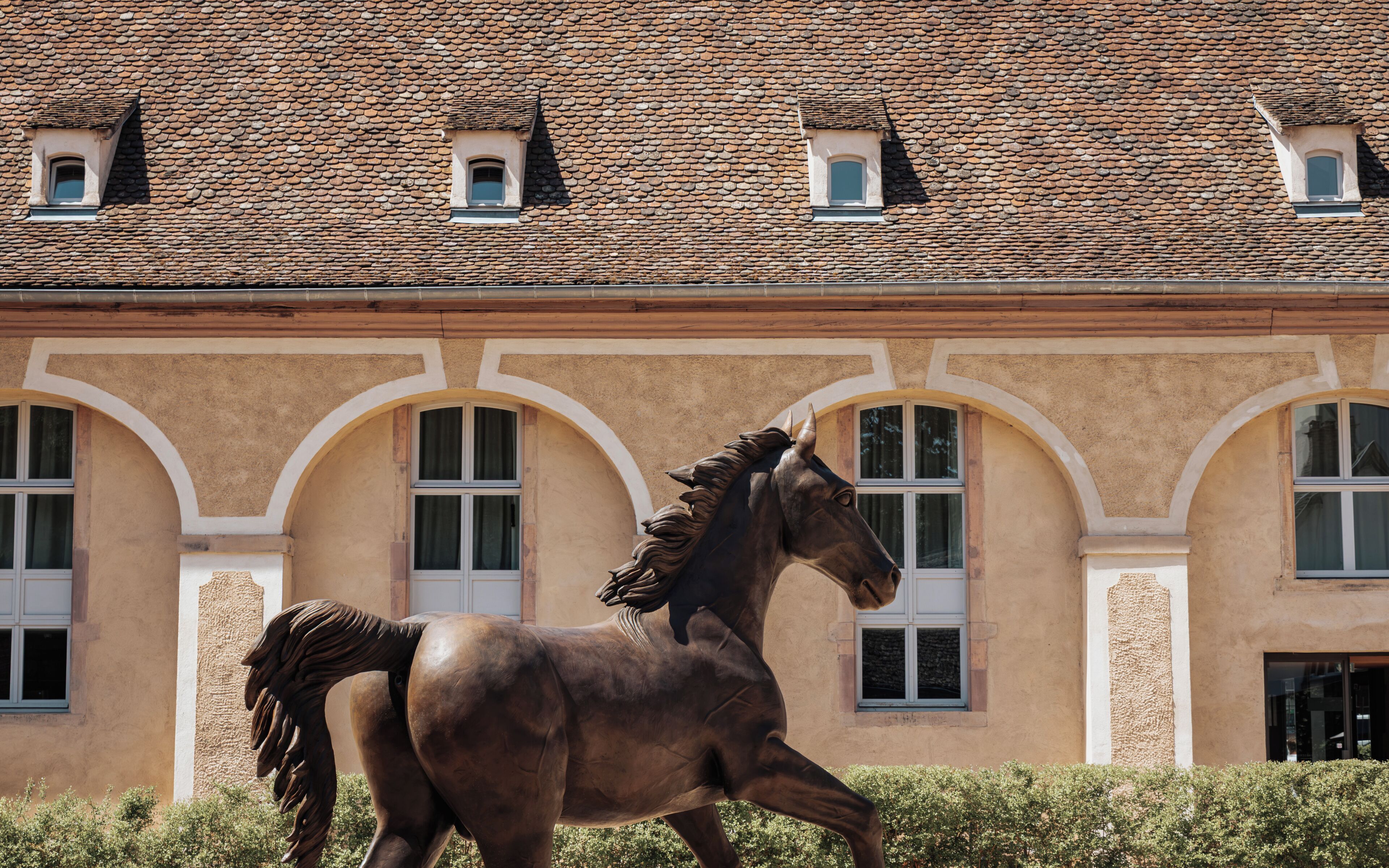 A horse statue in front of a building with a tiled roof and arched windows.