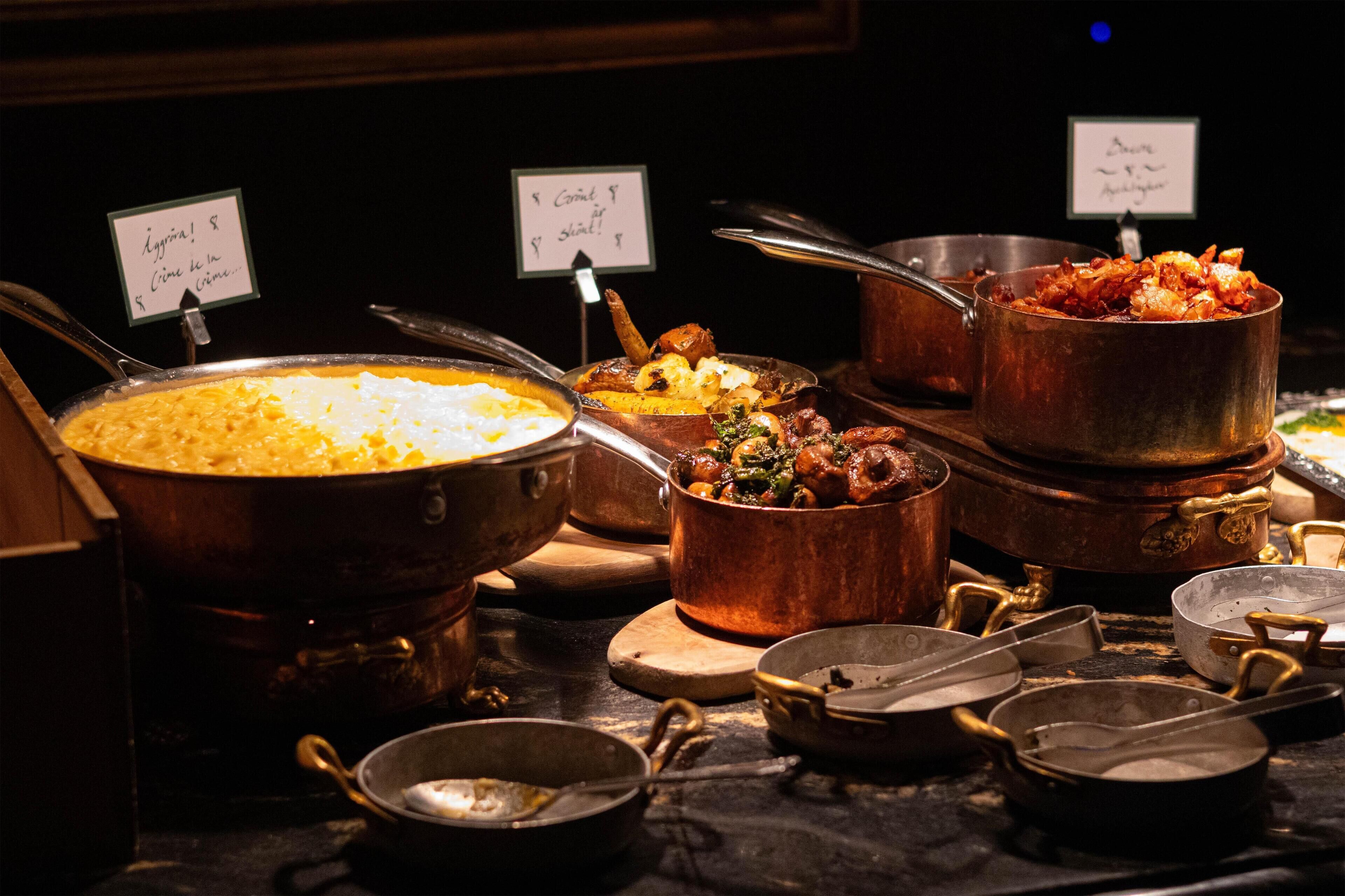 A buffet with various dishes in copper pots, including a large pot of soup and a pot of meat.