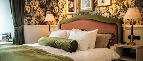 Una cama bien hecha con ropa de cama verde y blanca, un fondo de papel tapiz floral y dos lámparas fijadas a la pared.