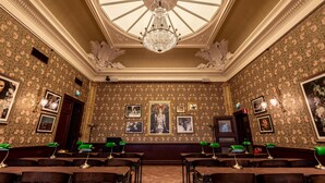 Un gran salón con papel tapiz ornamentado, una araña y cuadros enmarcados en las paredes.