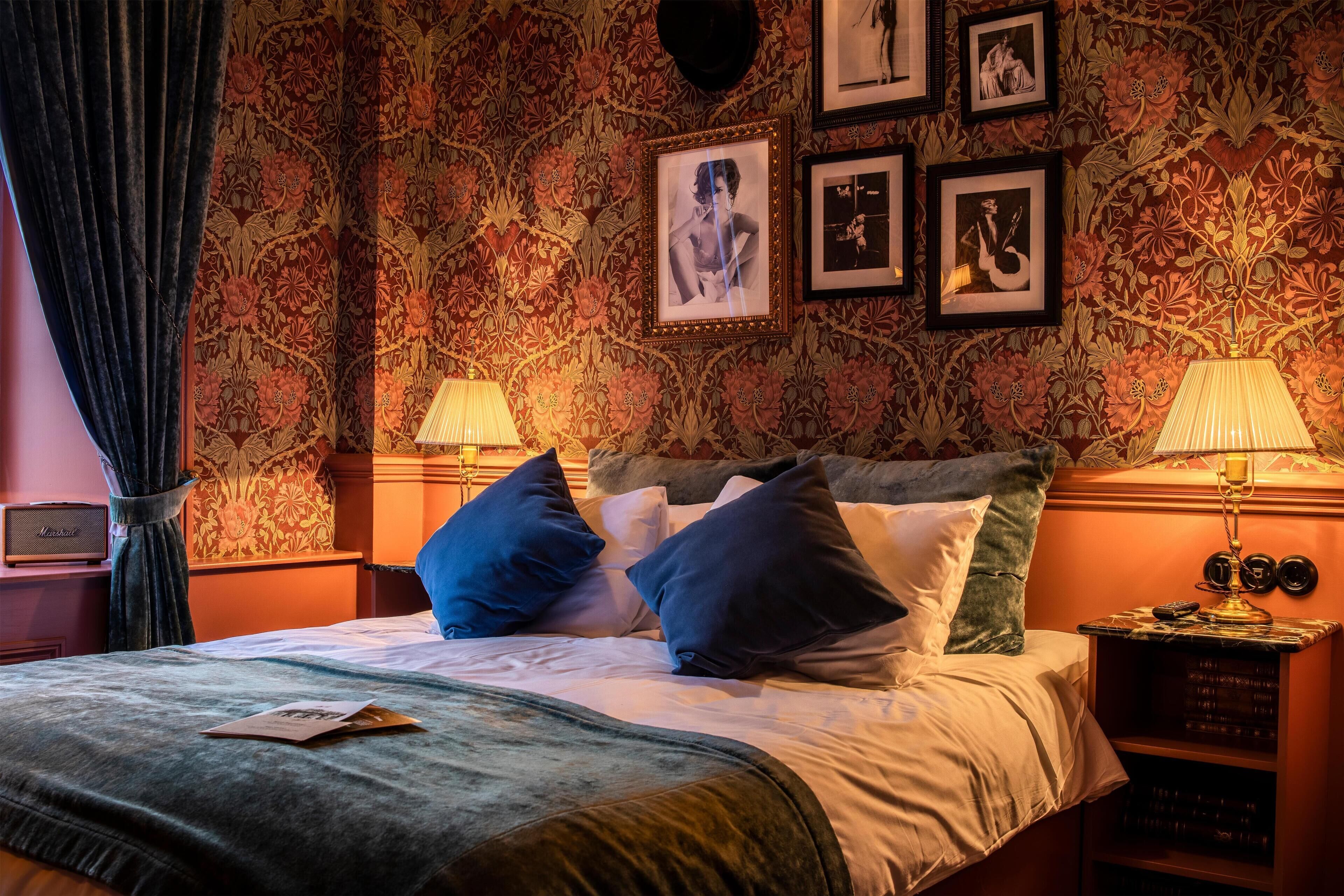 A hotel room with a bed, pillows, a lamp, a nightstand, and a wall with framed pictures.