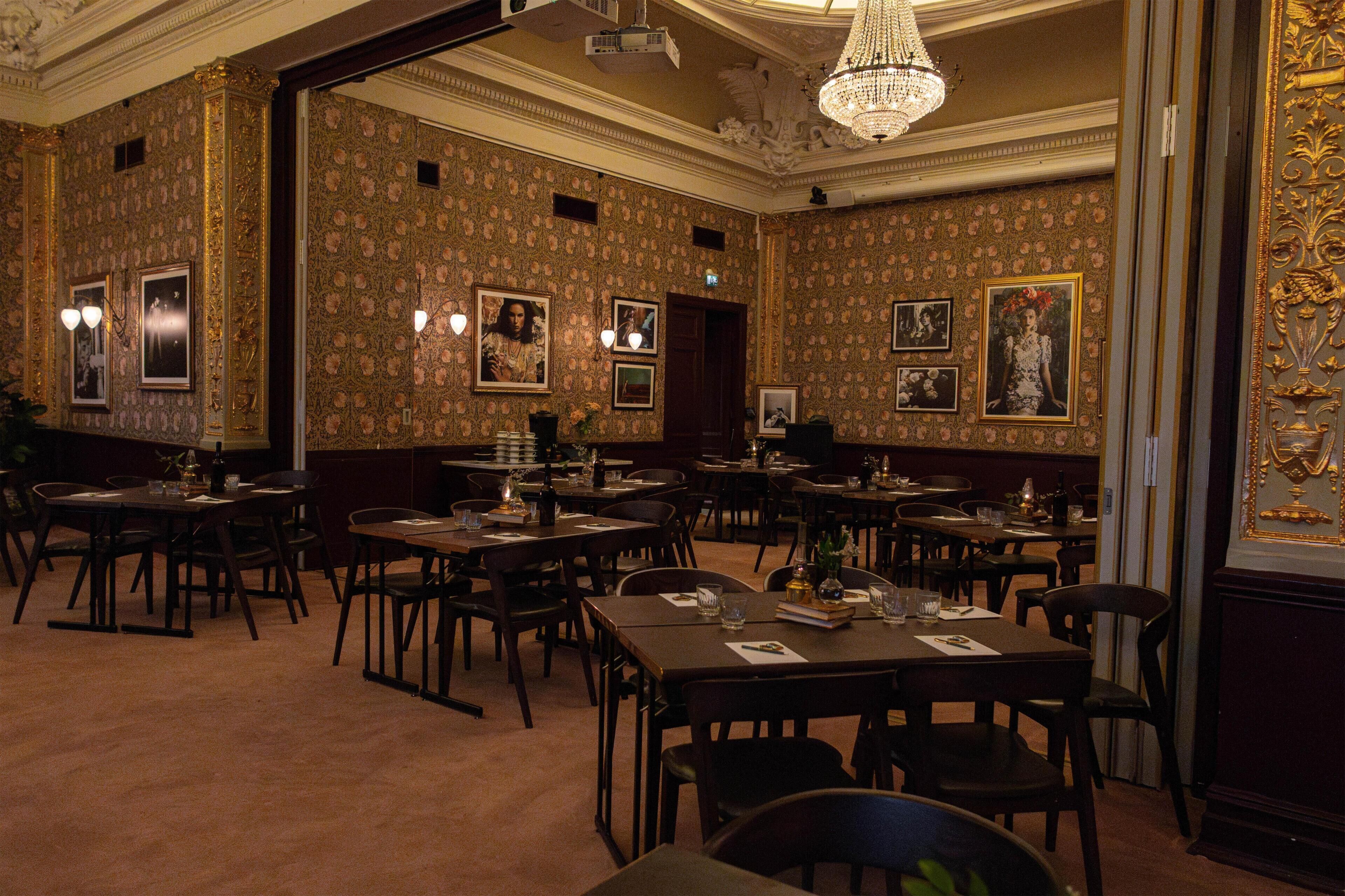 Ein formeller Speisesaal mit aufwändiger Tapete, Kronleuchtern und gerahmten Bildern an den Wänden.