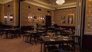 Ein formeller Speisesaal mit aufwändiger Tapete, Kronleuchtern und gerahmten Bildern an den Wänden.