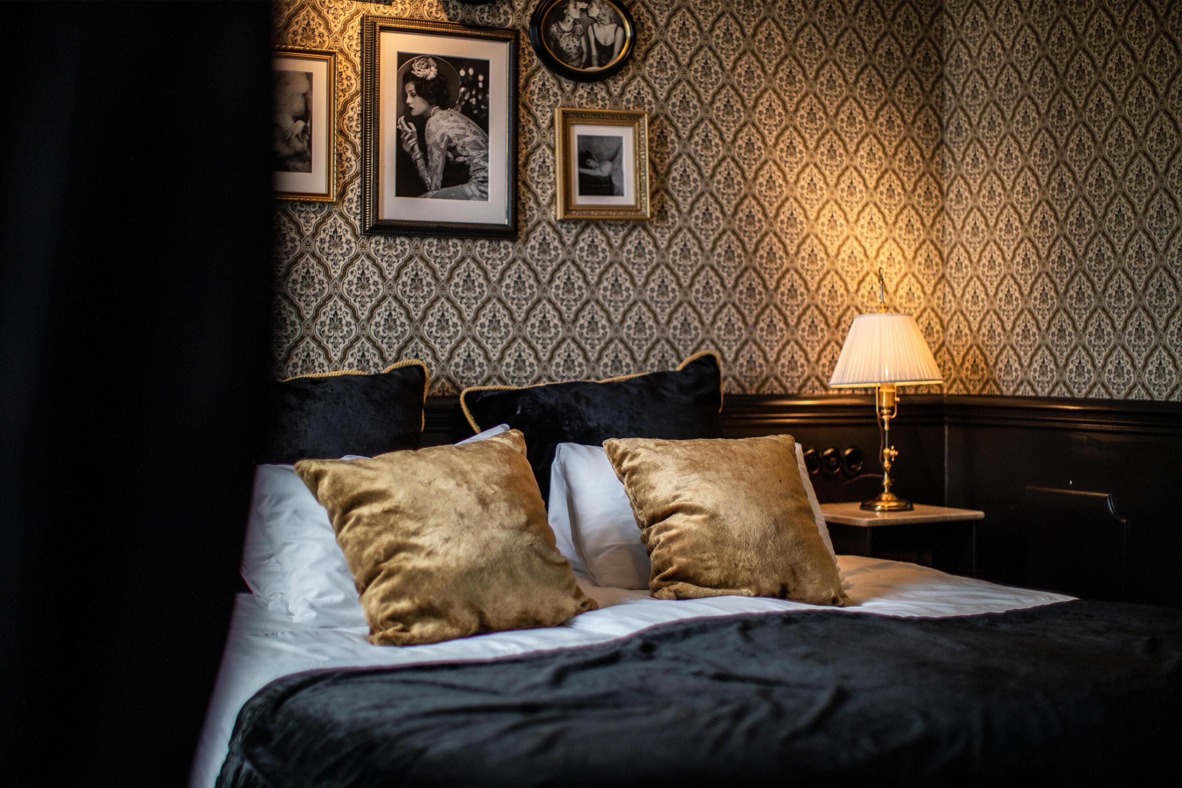 A neatly made bed with a black and white patterned headboard, two gold pillows, and a bedside table with a lamp.