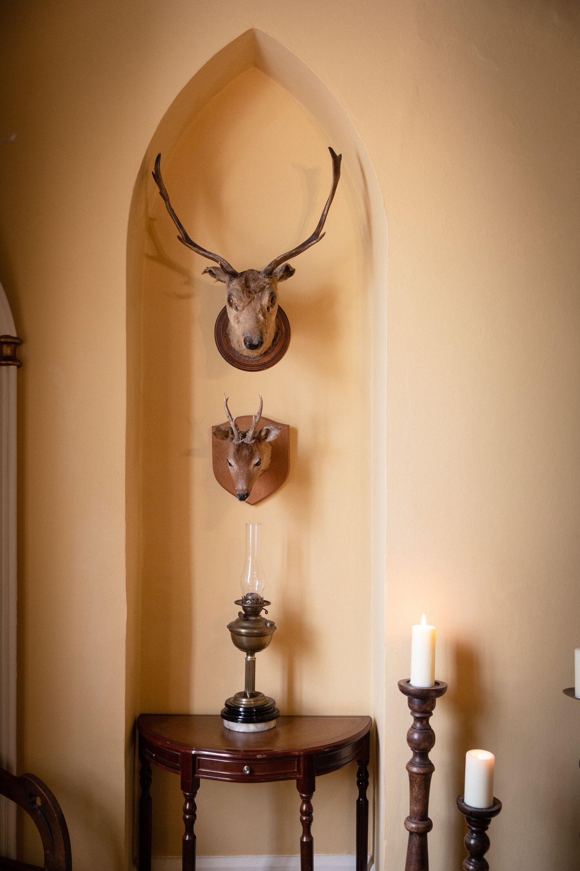 A wall-mounted deer head with antlers, a candle holder with a lit candle, and a small table with a candle.