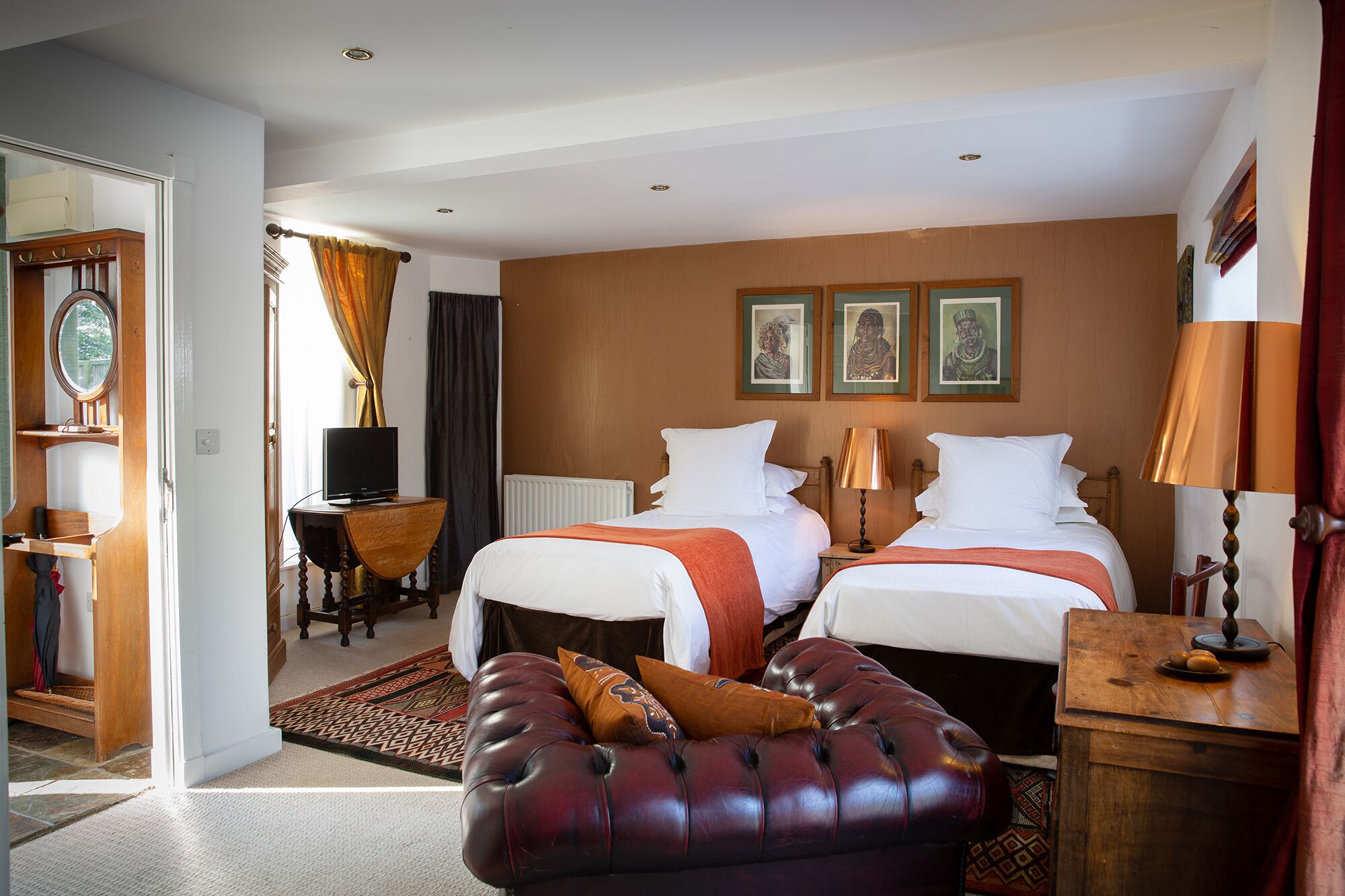 A hotel room with two beds, a desk, a television, and a leather ottoman.