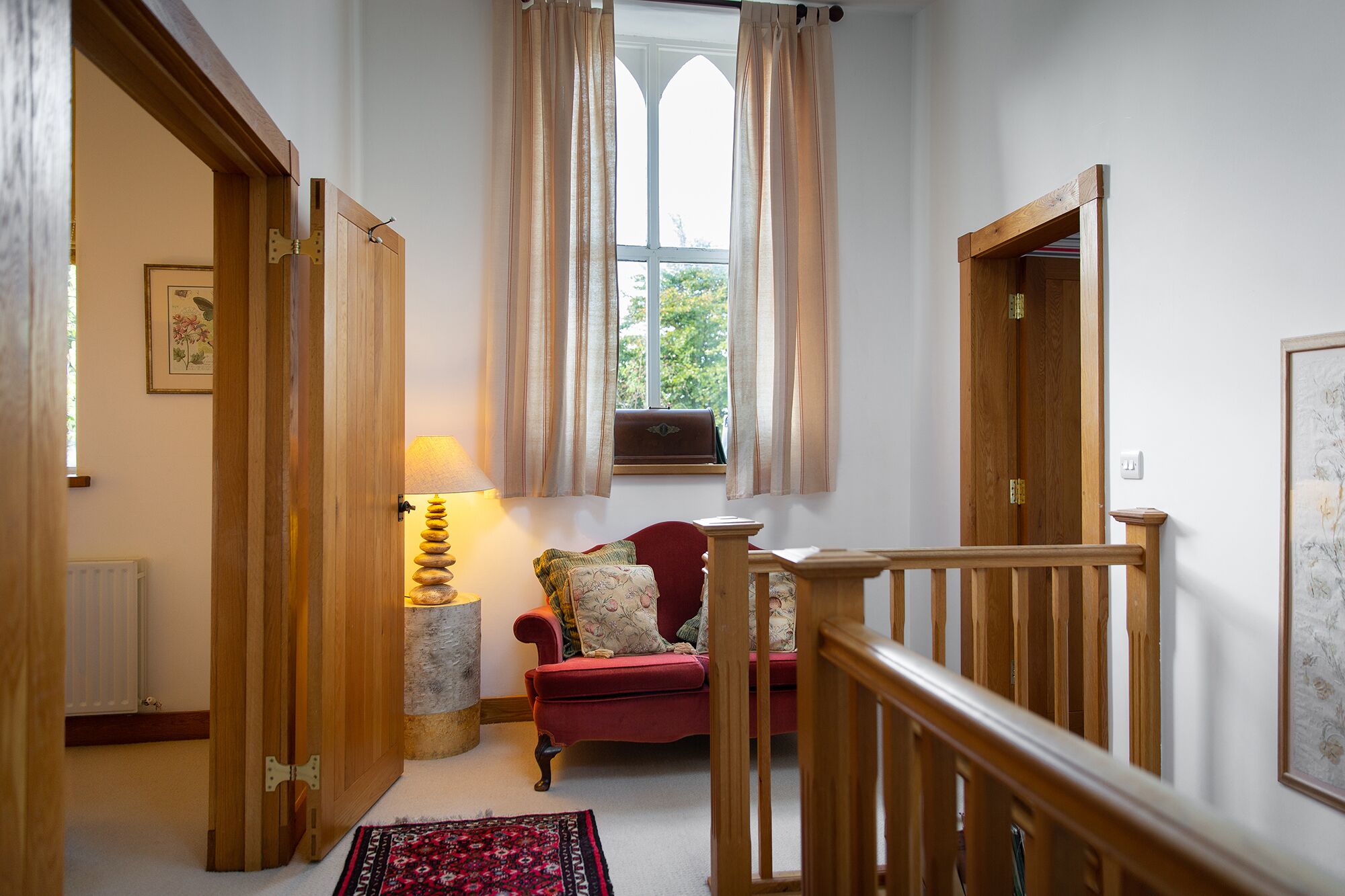 A cozy room with a red armchair, a wooden staircase, and a window with curtains.