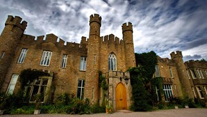 A historic stone castle with multiple towers, arched windows, and a large wooden door. - Augill Castle (Kirkby Stephen)