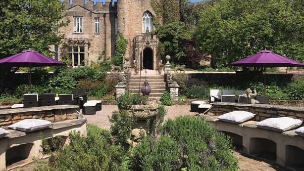 A historic building with a central tower, surrounded by lush greenery and outdoor seating areas with umbrellas. - Augill Castle (Kirkby Stephen)