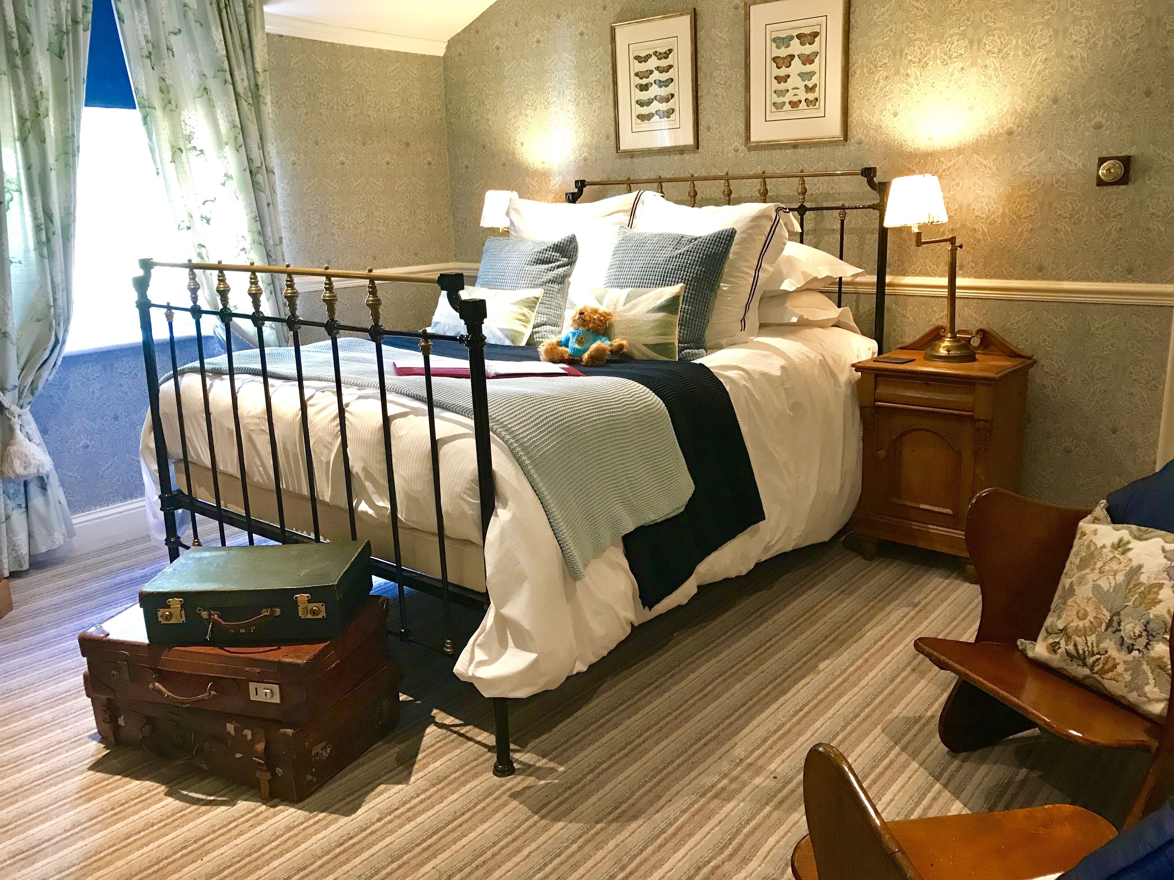 A neatly made bed with a headboard, a bedside lamp, a wooden nightstand, and a suitcase on the floor.