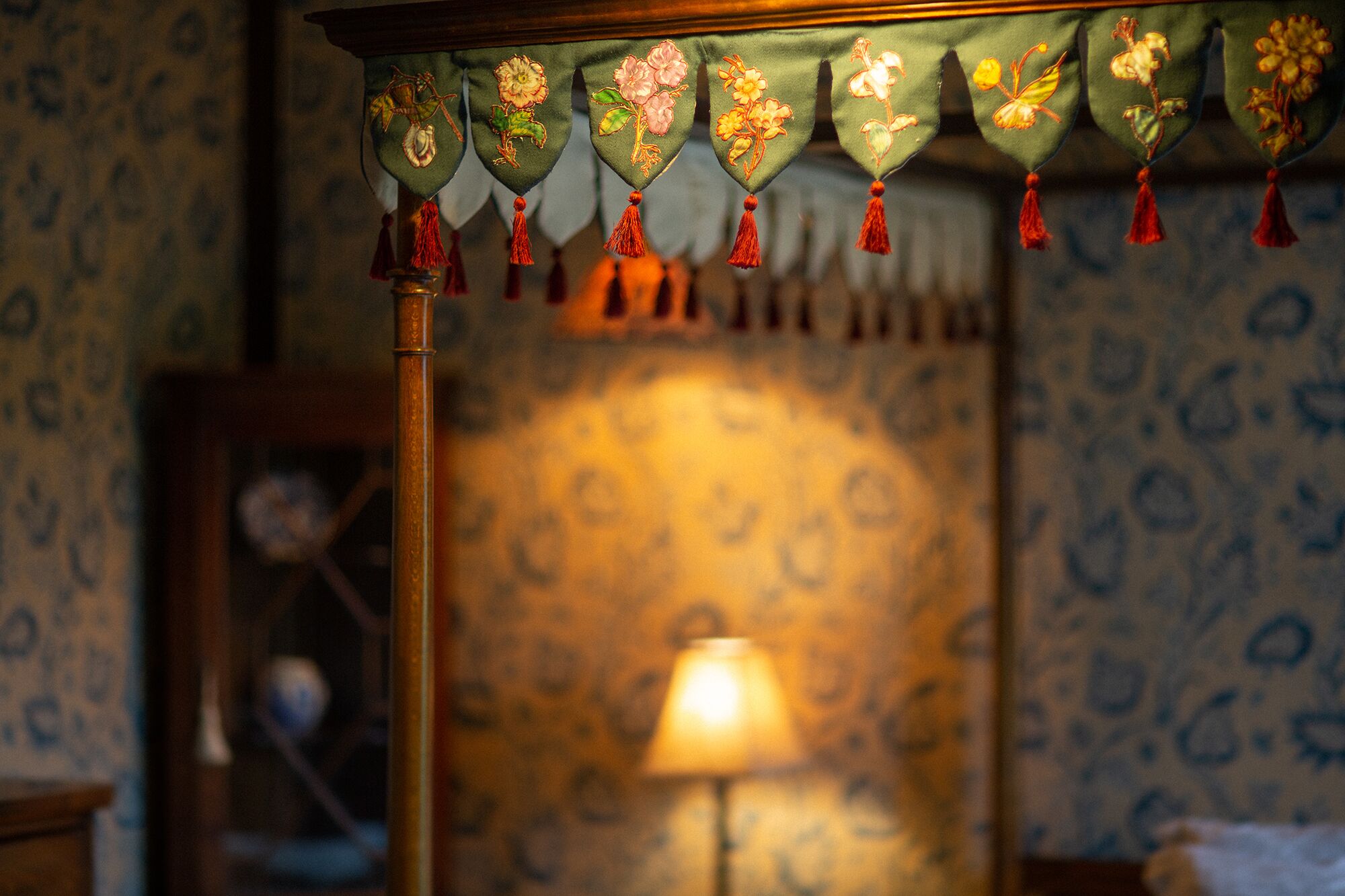 Une pièce avec un papier peint à motifs, une lampe et une décoration murale ornée de glands.
