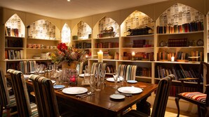 A dining area with a wooden table set for four, surrounded by striped chairs. Bookshelves line the walls, filled with books and decorative items. - Augill Castle (Kirkby Stephen)
