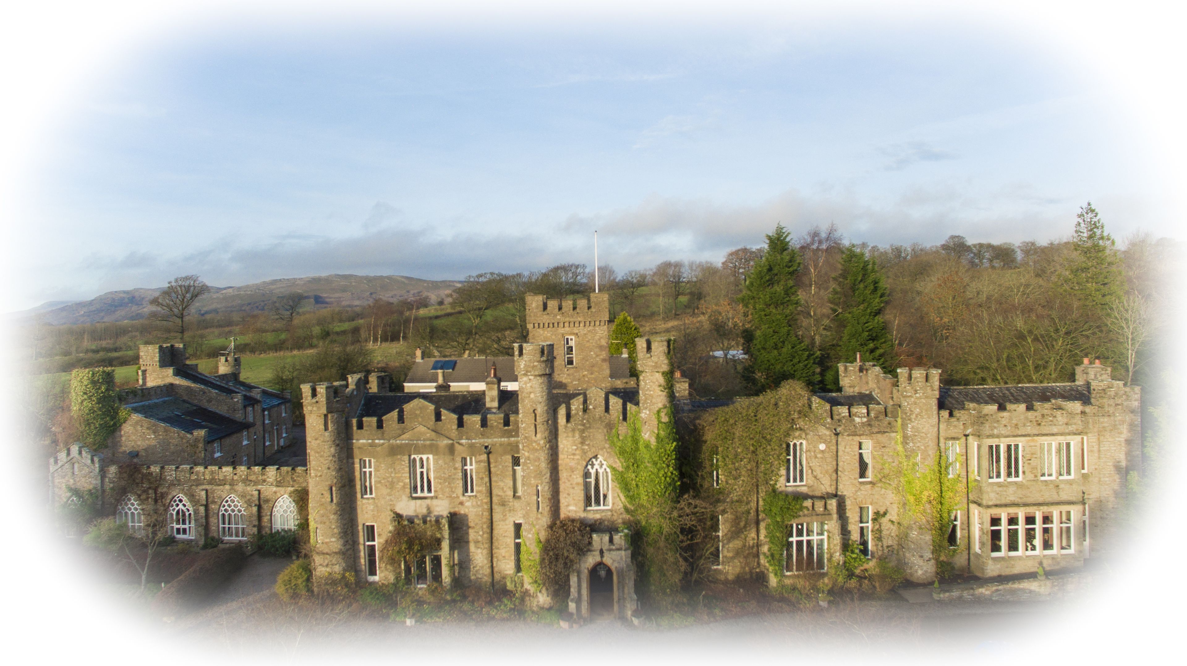 A historic stone castle with multiple towers and arched windows, surrounded by trees and hills.