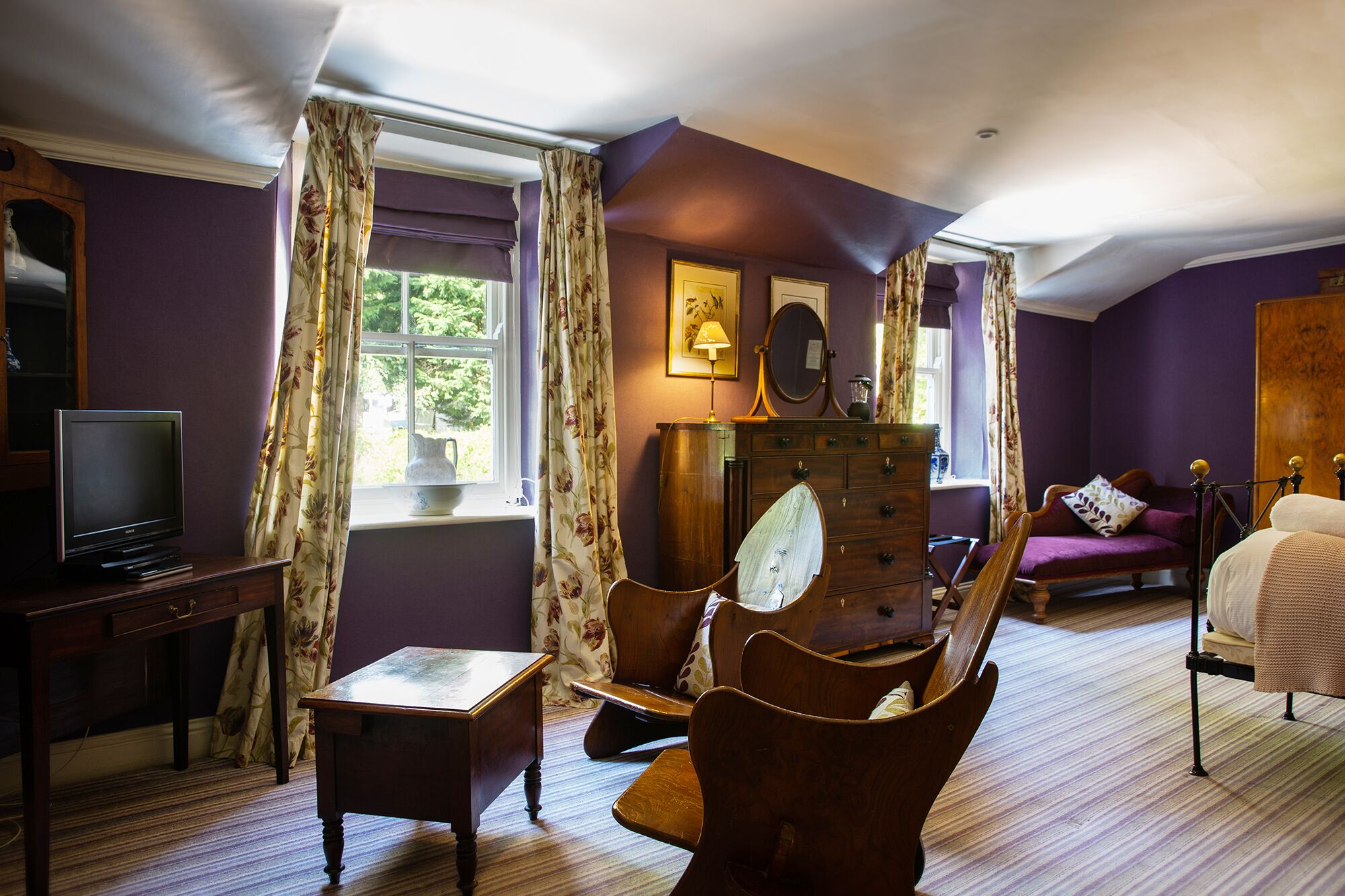 A room with a wooden dresser, a television, a chair, and a bed.