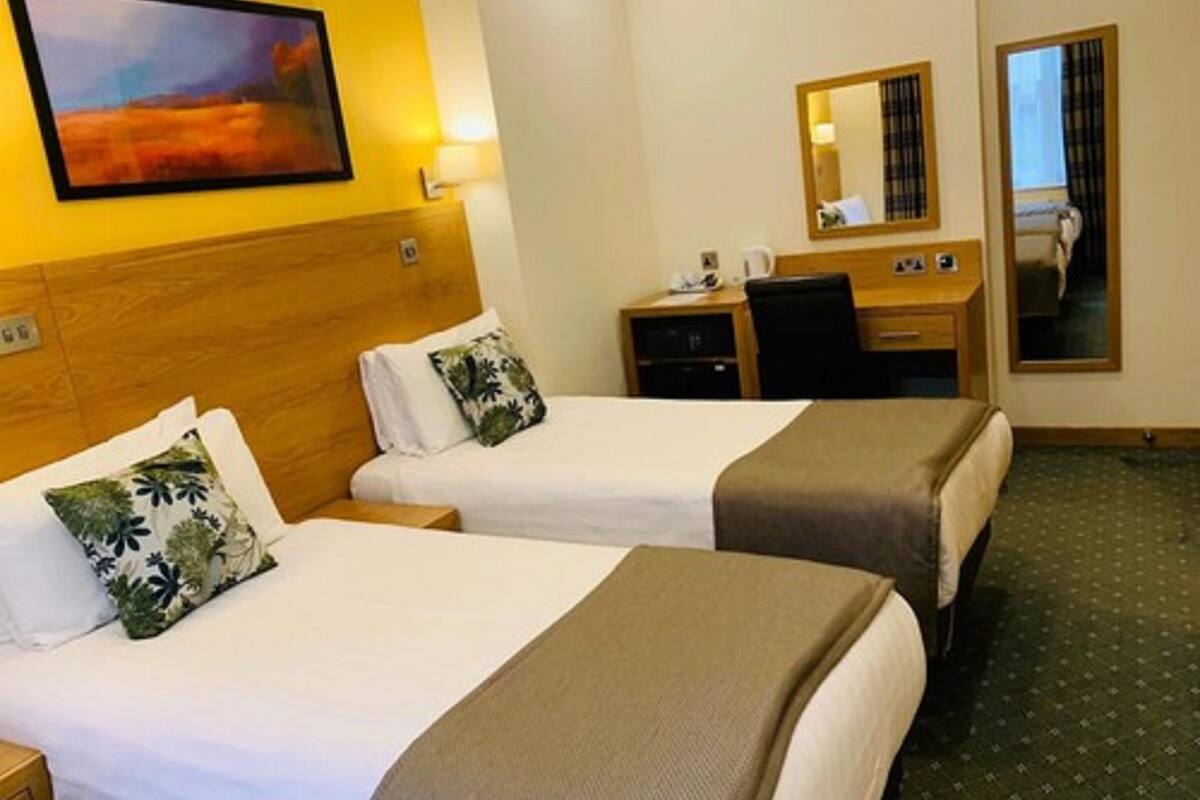 A hotel room with two beds, a desk, a chair, a mirror, and a painting on the wall.