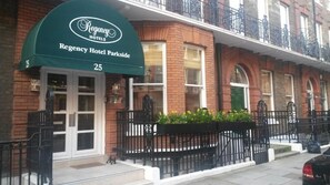 Hotel Regency Parkside con toldo verde, fachada de ladrillo y cerca de hierro forjado negro.