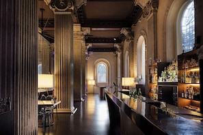 A bar area with marble columns, a long counter, and a view of a large arched window. - Palazzo Montemartini Rome, A Radisson Collection Hotel (Rome)
