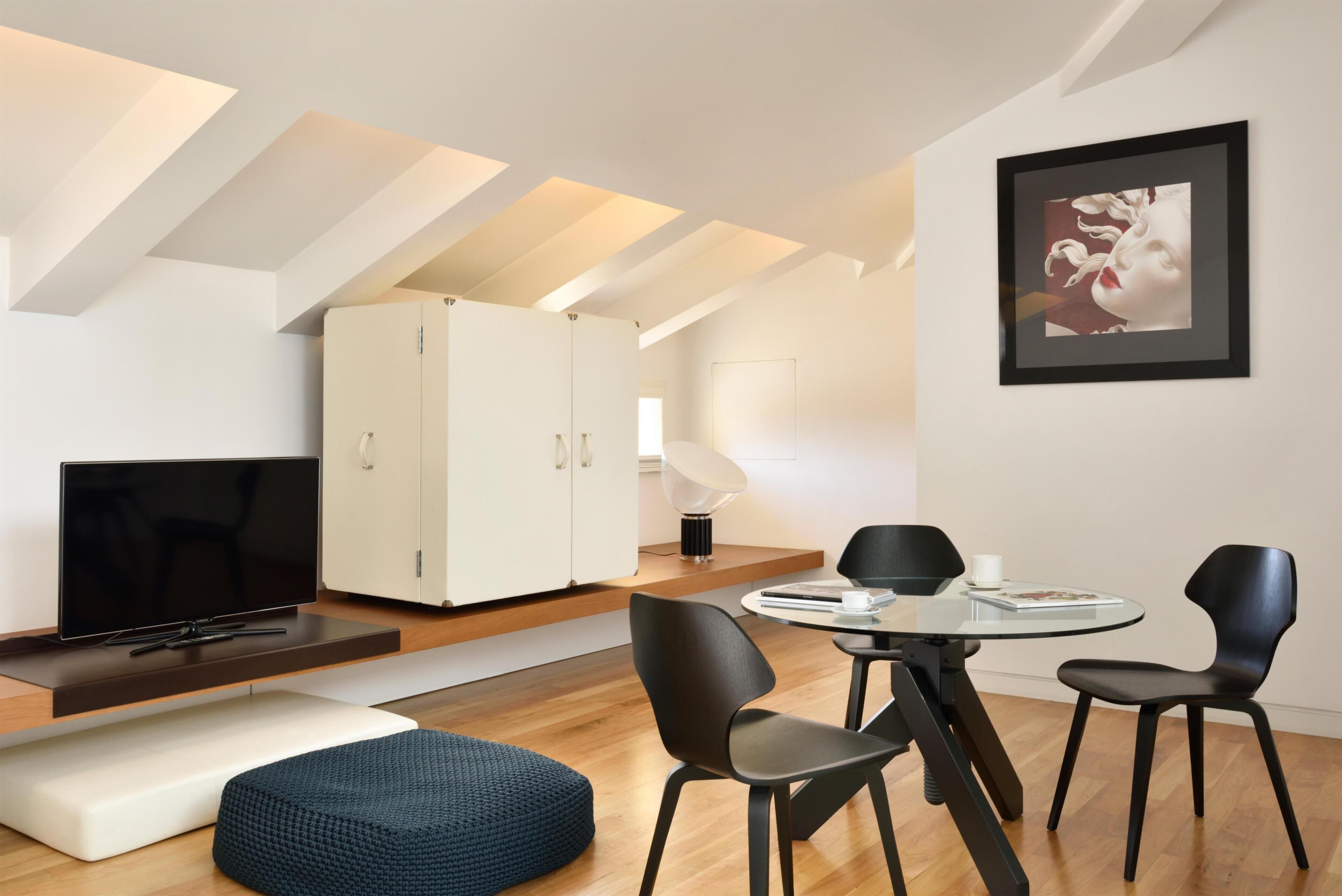 A modern living space with a flat-screen TV, a dining table with chairs, a sofa, a large cabinet, and a framed artwork on the wall.
