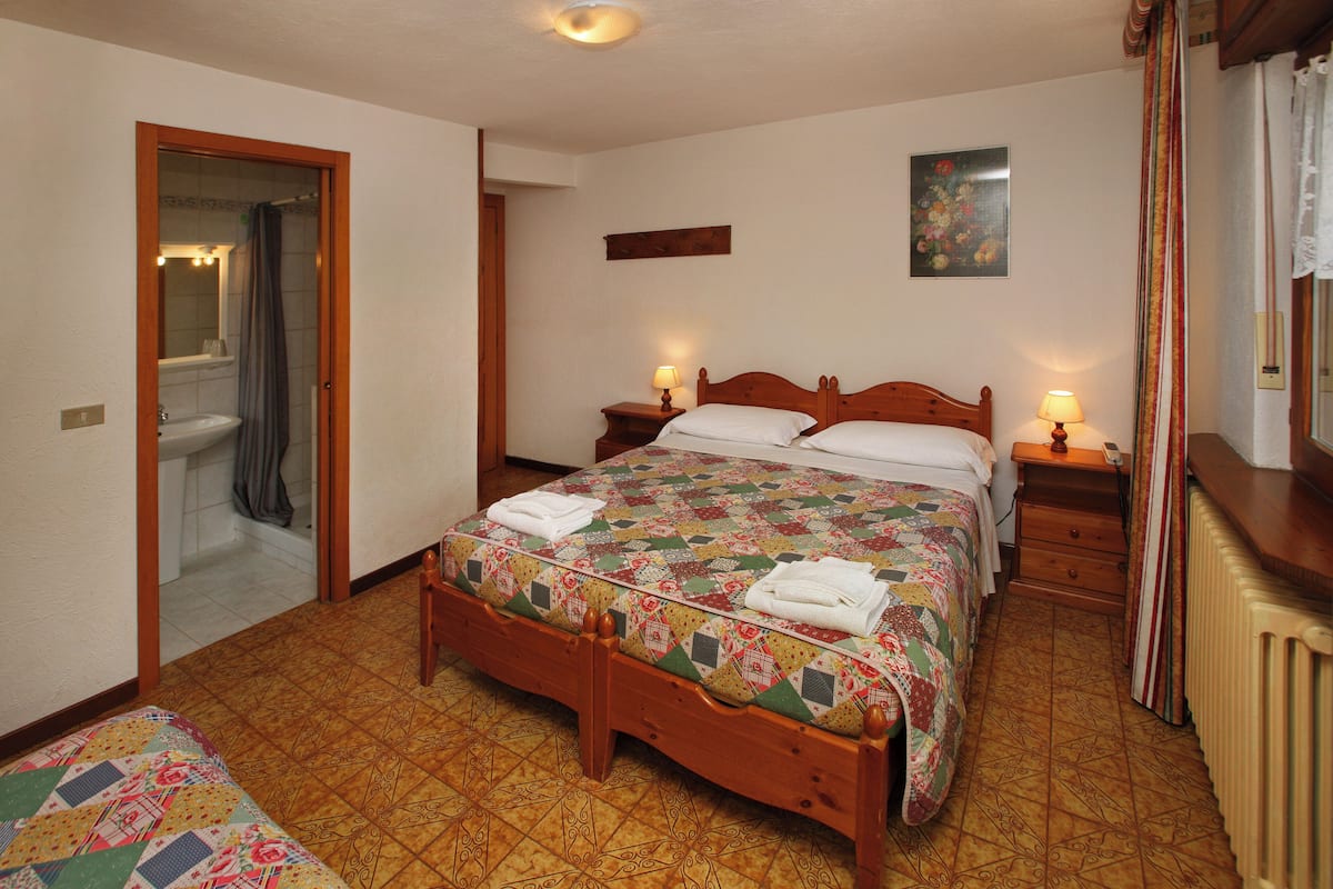 A bedroom with a wooden bed, two bedside tables with lamps, a radiator, and a bathroom visible through an open door.
