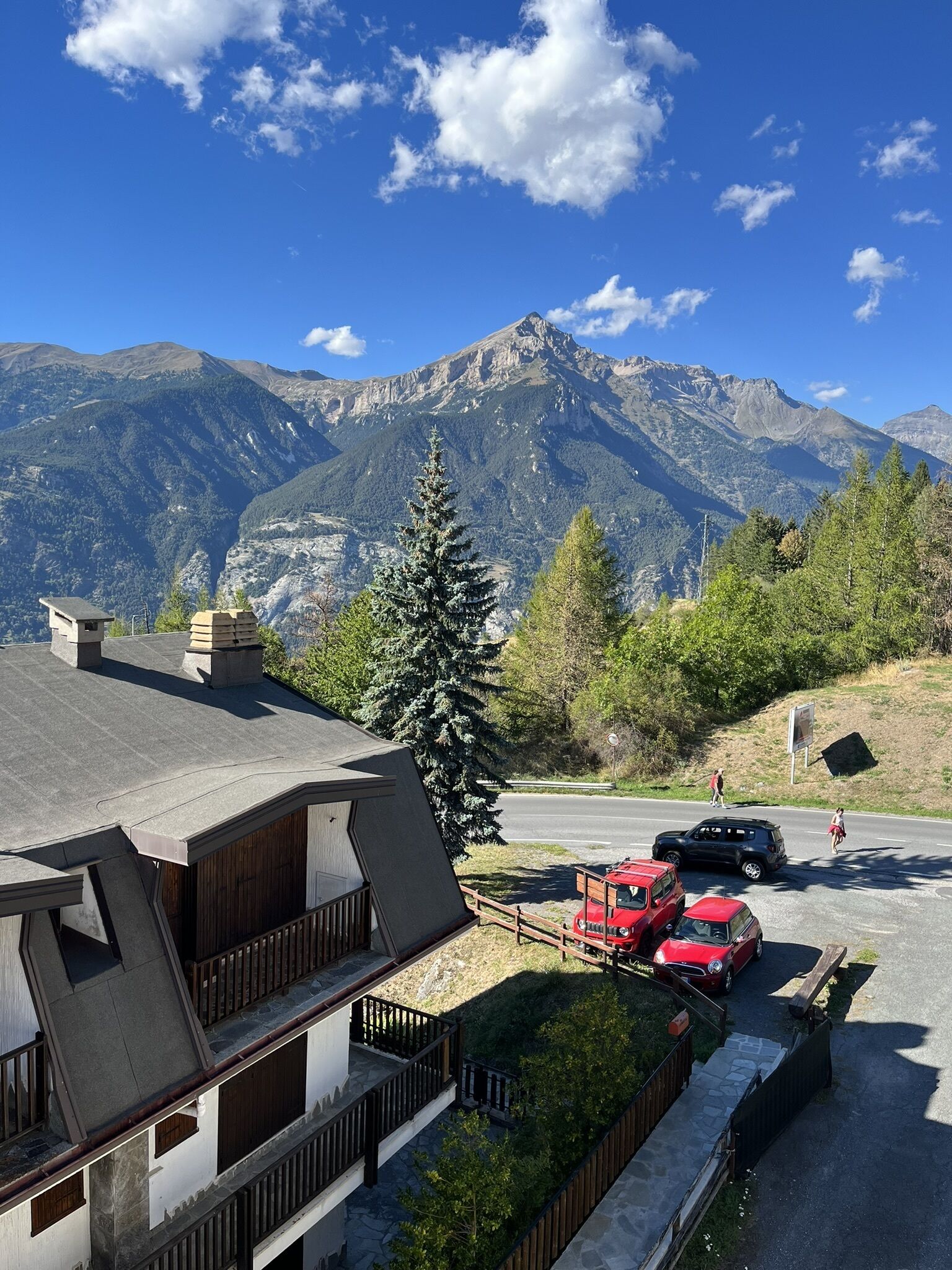 A mountain cabin with a sloped roof, a wooden deck, and a stone wall.