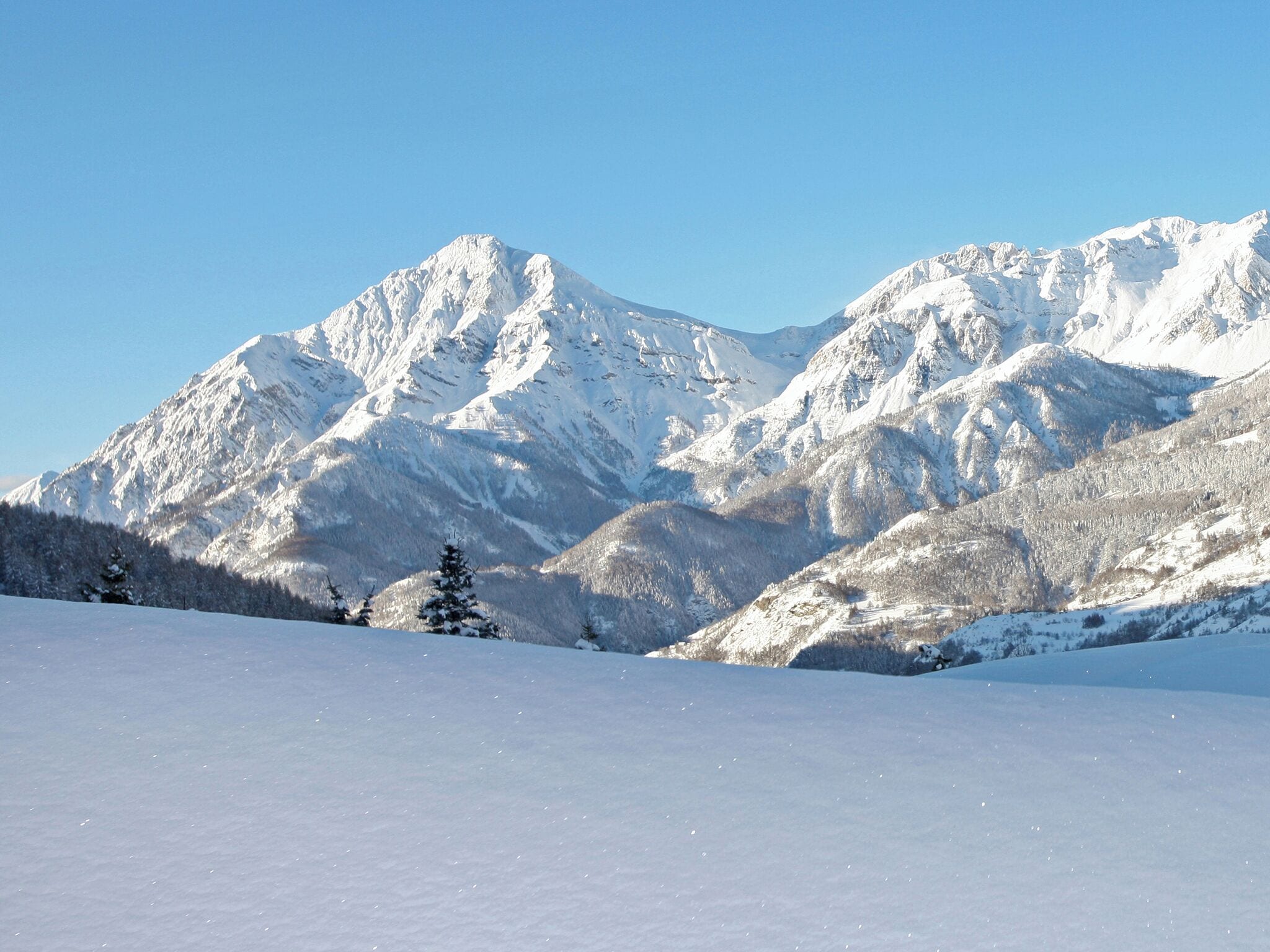 Paisaje montañoso cubierto de nieve con cielos despejados.