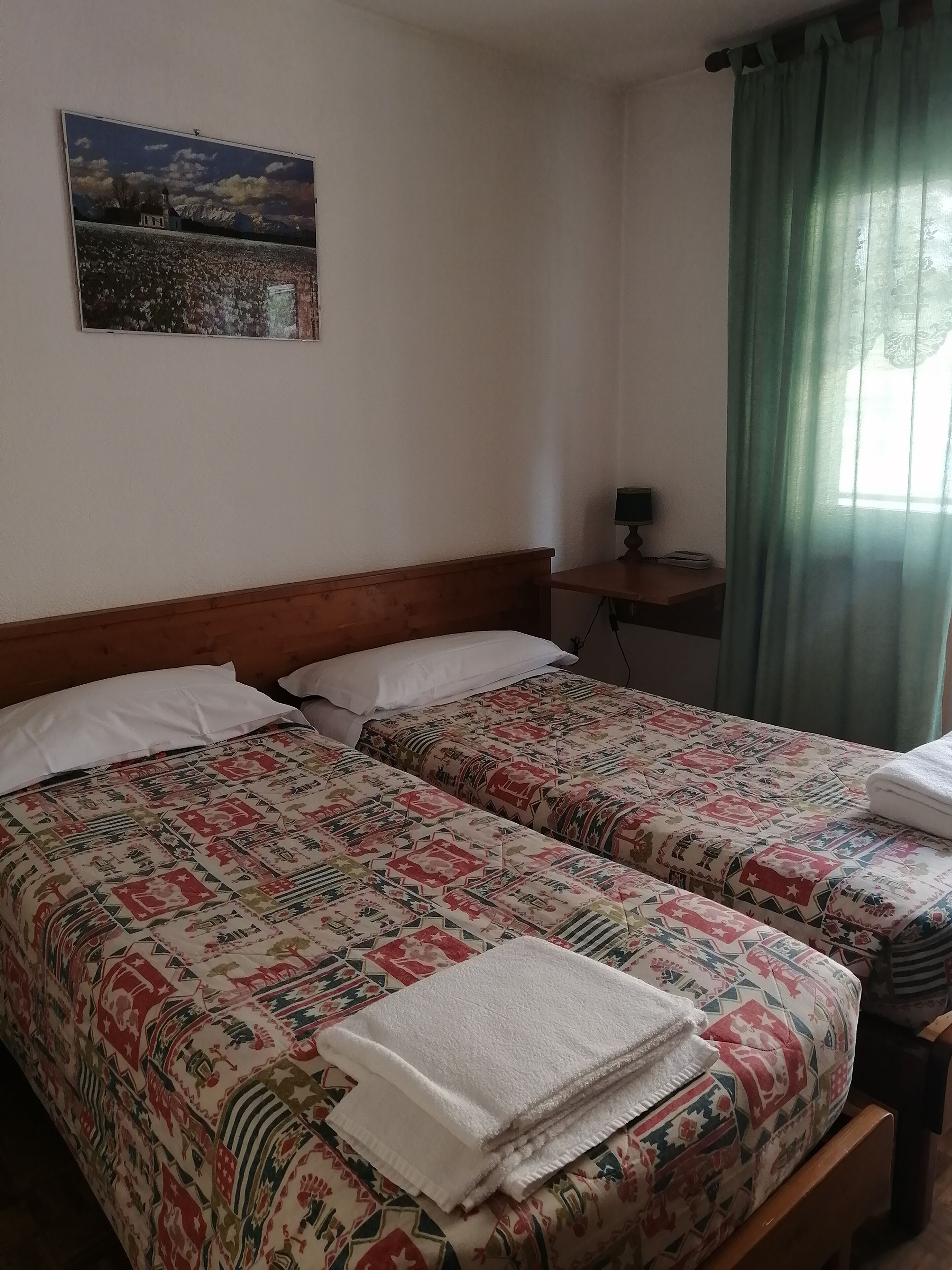 A hotel room with two beds, a nightstand, a lamp, and a painting on the wall.