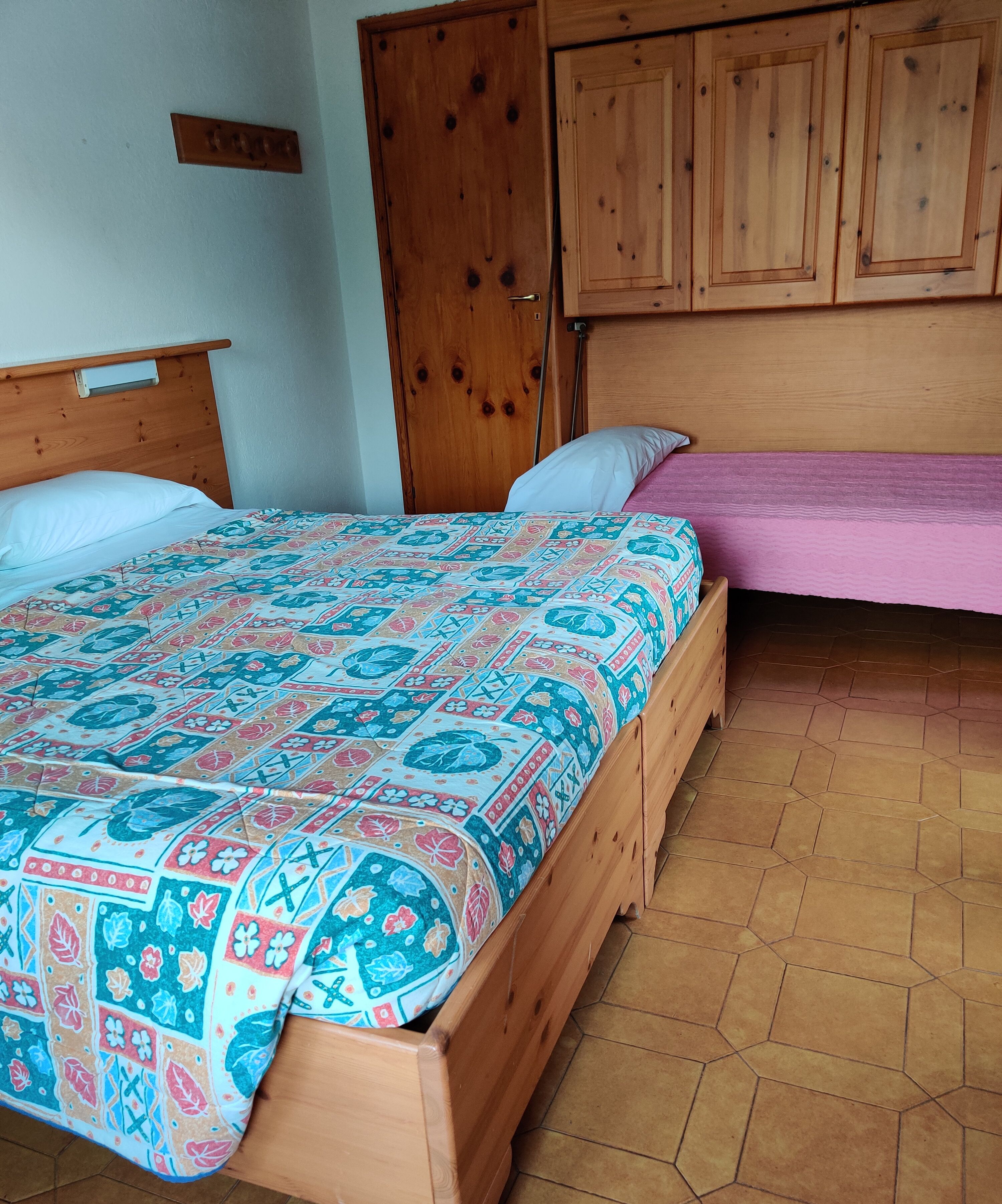 A bedroom with a wooden bed, a smaller bed with a pink bedspread, and a wooden wardrobe.